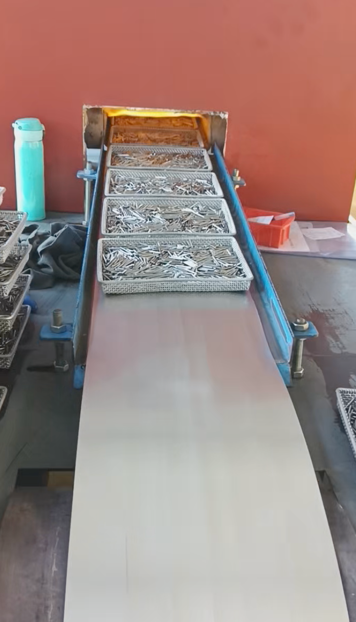 Workpiece trays on the steel conveyor beside the furnace opening